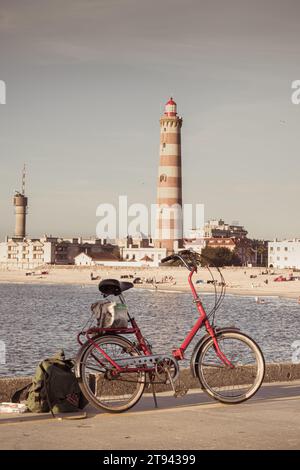 Ein rotes Fahrrad steht und Costa Nova Leuchtturm, Aveiro, Portugal Stockfoto