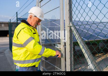 Elektroingenieur in Sicherheitsausrüstung öffnet ein Tor zu einem Solarfeld Stockfoto