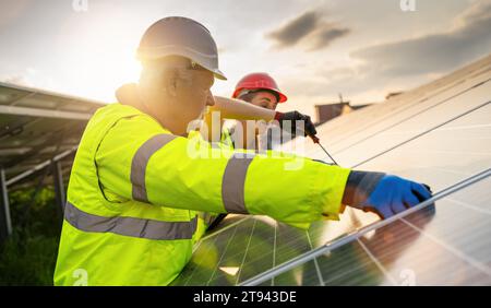 Team von Ingenieuren, die an der Wartung von Solarpaneelen bei Sonnenuntergang arbeiten. Alternatives energetisches ökologisches Konzeptbild. Stockfoto
