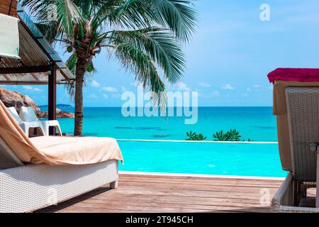 Liegestühle in der Nähe des Hotelpools mit Blick auf das Meer und tropisches Grün. Stockfoto