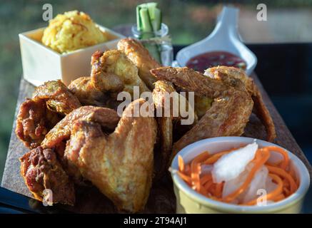 Hausgemachte gebratene Hähnchenflügel serviert mit köstlichem gelbem Jasminreis (Hühnchen Biryani), eingelegte Karotten und Rettich, Gurkenstangen und süßen Chili Stockfoto