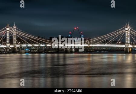 London, Großbritannien - 20. November 2023 - nächtlicher Blick auf die Albert Bridge mit Flutlicht von der Chelsea Bridge mit der Reflexion des Lichts in sehr ruhigem Wasser. Leuchtet A auf Stockfoto