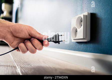 Steckdose, Stecker und Steckdose. Mann, der das Kabel aussteckt oder in der Hand hält. Sparen Sie Energie. Strom von der Hauswand. Stockfoto