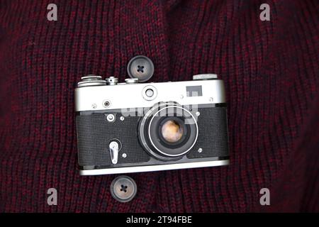 Retro Film Fotokamera auf rotem gestricktem Pullover Hintergrund. Alte Retro-Kamera auf abstraktem Vintage-Hintergrund. Nahaufnahme Stockfoto