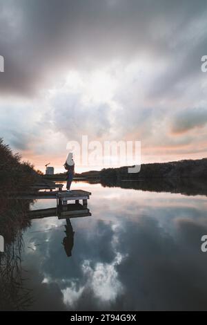 Dame im Alter von 20-25 Jahren, die auf einem hölzernen Pier an einem Teich stand und den Sonnenuntergang über der Stadt Oostende im Westen Belgiens beobachtete. Dramatischer rot-oranger Himmel. Stockfoto