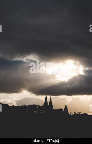 Die Sonne bricht bei Sonnenuntergang durch die Wolken und sendet ihre Strahlen auf Gebäude in Kortrijk, Belgien. Stockfoto