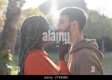 Ein junger Mann und eine junge Frau teilen einen zärtlichen Moment mit dem goldenen Glanz des Sonnenuntergangs hinter ihnen, was auf Romantik hindeutet Stockfoto