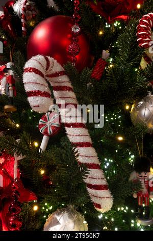Glitzernde dekorative rote und weiße Zuckerrohrdekoration und Kugeln auf einem grünen Weihnachtsbaum für das Konzept der Weihnachtsgrüße Stockfoto