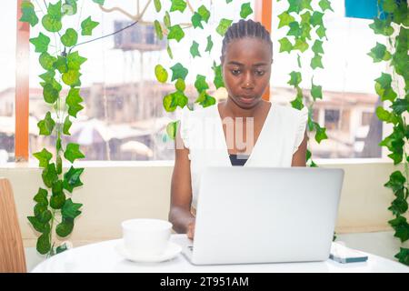 Stilvolle Frau, die am Laptop arbeitet, ein strahlendes Lächeln, sie mühelos Multitasking auf ihrem Laptop Stockfoto