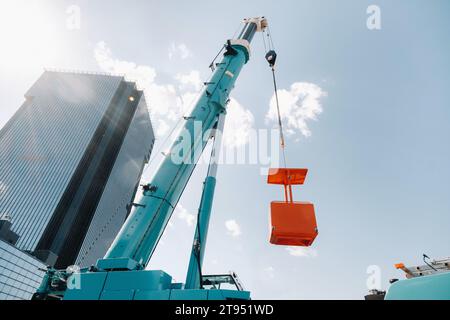 Ein großer blauer LKW-Kran steht auf einem Gelände in der Nähe eines großen modernen Gebäudes betriebsbereit. Der größte Lkw-Kran mit gelber Wiege zum Lösen von c Stockfoto