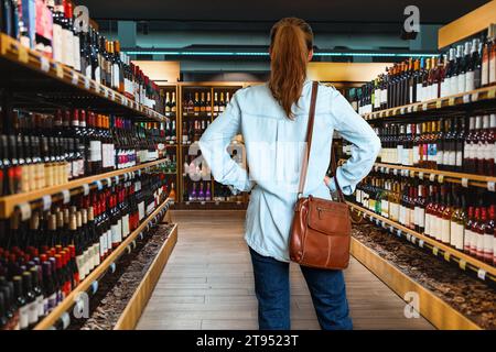 Rückansicht einer Verbraucherin, die im Spirituosengeschäft steht und Wein wählt. Stockfoto