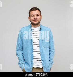 Porträt eines Mannes, der lässig in Jeanshemd und gestreiftem T-Shirt trägt, lächelt vor einem schlichten Hintergrund im Studio. Stockfoto