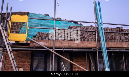 Gerüste rund um das Haus für sicheren Zugang zum Dach, Fliesen entfernt und gestapelt, bereit zum Wiedereinbau. Stockfoto