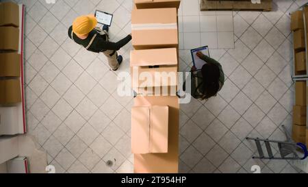 Top-Down-Ansicht der Koordinatoren der Lagerlogistik, die Papppakete parallel untersuchen und die Ergebnisse vergleichen. Mitarbeiter im Vertriebszentrum sorgen dafür, dass Lagerbestände und Lagerbestände gut organisiert sind Stockfoto