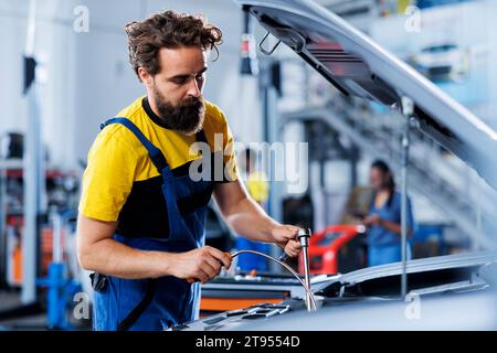 Zertifizierter Ingenieur, der in der Werkstatt alte Getriebeflüssigkeit mit einem Ölabzieher durch ein neues ersetzt. Werkstattarbeiter mit professioneller Ausrüstung für die Fahrzeugwartung Stockfoto