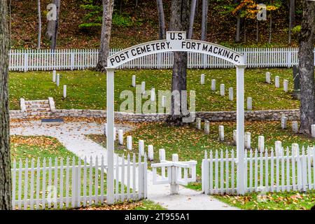 Ein weißer Torbogen mit der Aufschrift "Post Cemetery, U.S. Fort Mackinac" markiert den Eingang zum kleinen Militärfriedhof hinter dem alten Fort Mackinac, das 1780 von den Briten gegründet wurde. Reihen von schlichten weißen Grabsteinen stehen zwischen den Bäumen. Mackinac Island, Michigan, Vereinigte Staaten. Stockfoto