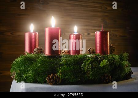 Zum dritten Adventsfest drei brennende Kerzen auf einem Adventskranz vor hölzernem Hintergrund Stockfoto