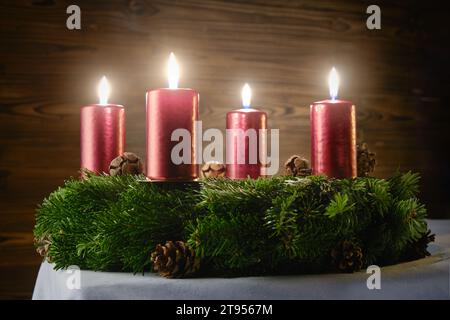 Für den vierten Adventskranz vier brennende Kerzen auf einem Adventskranz vor hölzernem Hintergrund Stockfoto