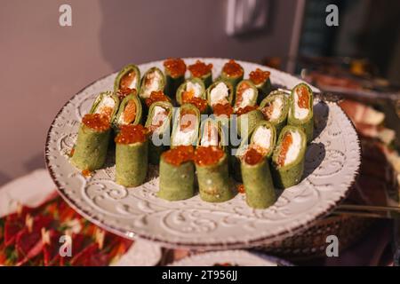 Festliche Vorspeisen auf Empfängen. Spinatkrabben rollt mit Kaviar, Lachs und Frischkäse darin. Teller mit herzhaften Meeresfrüchten-Pfannkuchenbrötchen mit Reh. Stockfoto