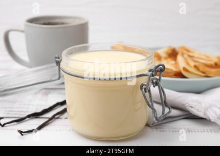 Leckere Kondensmilch im Glas, Crepes und Vanilleschoten auf weißem Holztisch, Nahaufnahme Stockfoto