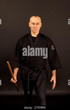 Porträt des Aikido-Sensei-Meisters mit schwarzem Sensei-Gürtel in Taekwondo-Kimono mit Bokken auf schwarzem Hintergrund. Traditioneller Samurai-Hakama-Kimono. Gesundheit Stockfoto