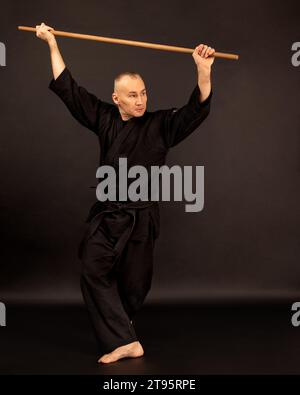 Porträt des Aikido-Sensei-Meisters mit schwarzem Sensei-Gürtel in Taekwondo-Kimono mit Bokken auf schwarzem Hintergrund. Traditioneller Samurai-Hakama-Kimono. Gesundheit Stockfoto