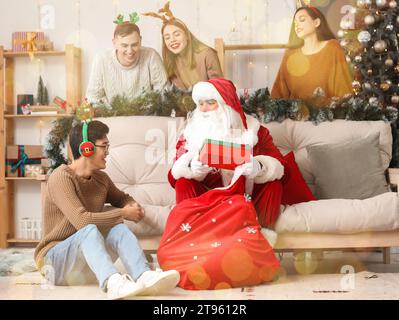 Weihnachtsmann schenkt jungen Leuten Weihnachtsgeschenke auf einer Party Stockfoto