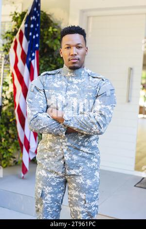 Männlicher afroamerikanischer Soldat, der mit Armen vor dem Haus steht, mit us-Flagge, Kopierraum Stockfoto