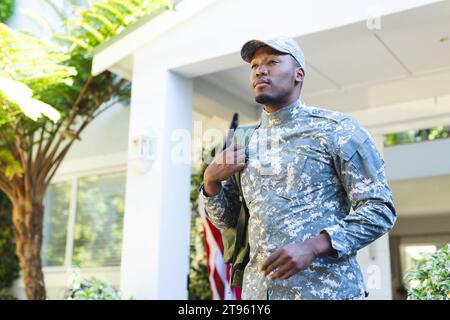 Fokussierter afroamerikanischer männlicher Soldat mit Mütze und Rucksack draußen mit us-Flagge, Kopierraum Stockfoto