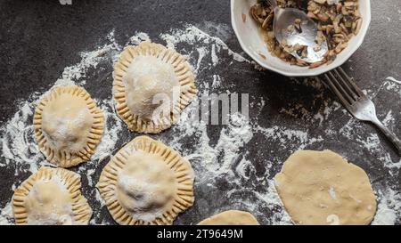 Herstellung glutenfreier Teigtaschen mit Pilzen und Zwiebeln. Dunkelgraue Arbeitsplatte mit Mehl bestreut. Hausgemacht. Stockfoto