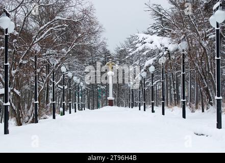 Parkstraße mit symmetrischen Lichtmasten und der Statue des Engels des Friedens. Bild von der verschneiten Magadan-Stadt im Winter, Russland. Stockfoto