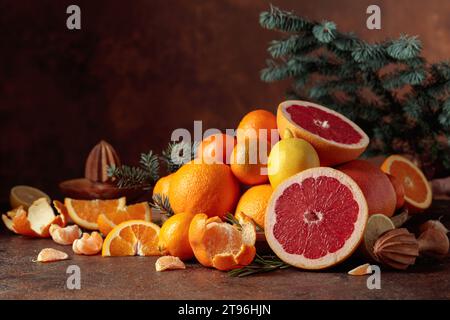 Zitrusfrüchte und Fichtenzweig auf braunem Hintergrund. Weihnachtliches Stillleben mit Orangen, Grapefruits, Zitronen und Mandarinen. Stockfoto