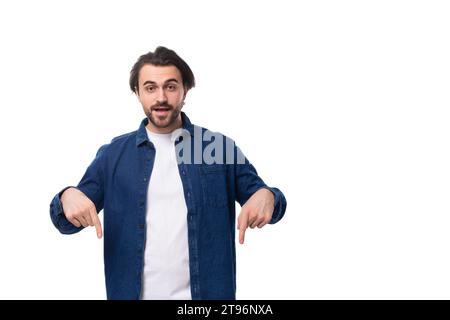 Hübscher junger brünette Mann in einem Jeansshirt zeigt mit der Hand auf einen leeren Platz auf weißem Hintergrund Stockfoto