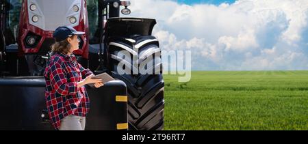 Landwirtin mit einem digitalen Tablet neben einem landwirtschaftlichen Traktor. Stockfoto