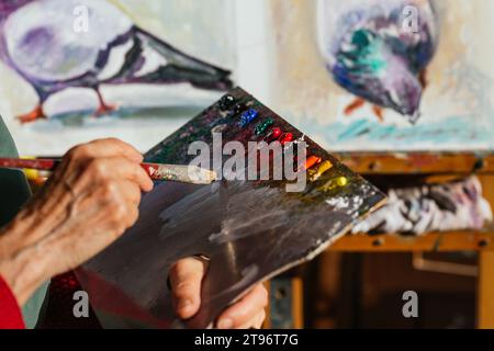 Von oben der Ernte unkenntlich ältere weibliche Malerin mischen Farben auf Farbpalette in der Kunstwerkstatt Stockfoto