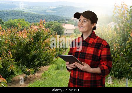 Eine Landwirtin untersucht den Garten der Früchte und sendet Daten vom Tablet an die Cloud. Intelligente Landwirtschaft und digitale Landwirtschaft. Stockfoto