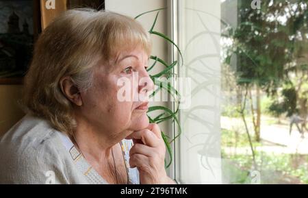 Traurige Seniorin, die aus dem Fenster schaut. Einsame alte Großmutter allein zu Hause Stockfoto