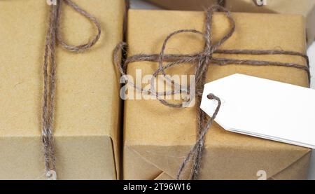 Leere Papierkarte auf handgefertigten braunen Geschenkkartons, die in handgefertigtes Papier gewickelt sind. Postkartenvorlage für Weihnachtsgrüße Stockfoto