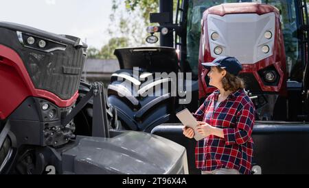 Landwirtin mit einem digitalen Tablet neben einem landwirtschaftlichen Traktor. Stockfoto