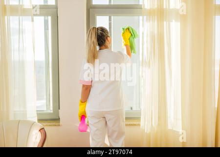 Bild des Zimmermädchens, das Fenster in einem Zimmer sauber macht. Stockfoto