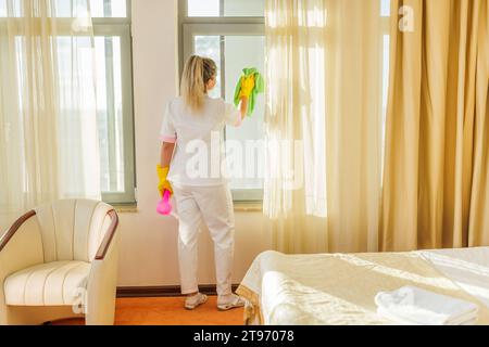 Bild des Zimmermädchens, das Fenster in einem Zimmer sauber macht. Stockfoto