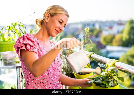 Glückliche Frau, die zu Hause auf dem Balkon im Garten arbeitet. Sie kümmert sich um ihre Erdbeerpflanze. Stockfoto