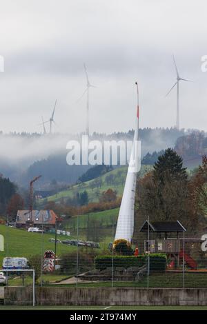 23. November 2023, Baden-Württemberg, Biberach: Auf einem sogenannten selbstfahrenden Transporter wird ein Windenergieschaufel montiert und durch das Dorf Prinzbach transportiert, während andere Windenergieanlagen im Hintergrund zu sehen sind. Insgesamt sollen drei 68 Meter lange Rotorblätter aus Biberach über eine Entfernung von rund sieben Kilometern transportiert werden. Nach Angaben des Energieversorgers Badenova sind millimetergenaue Arbeiten erforderlich, um sicherzustellen, dass die Rotorblätter die Baustelle unbeschädigt erreichen. An einigen Stellen entlang der Strecke muss eine Steigung von 12 Prozent gemeistert werden. Foto: Philipp Stockfoto