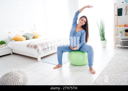 Foto einer charmanten, sportlichen Mama, die die Hände hebt, während sie sich aufwärmt, das Herz-Kreislauf-Training in der Wohnung drinnen Stockfoto