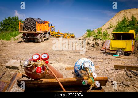 Rote und blaue Schweißgeräte, Sauerstoff- und Stickstofftanks mit Ventilen und Manometern, Acetylengaszylinder auf Metallstapeln im Gebäude Stockfoto