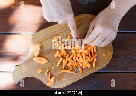 Die Frau schneidet Karotten auf einem hölzernen Schneidebrett Stockfoto