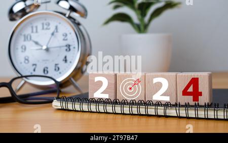 Holzblöcke mit den Buchstaben 2024 mit Kalender und Wecker auf hölzernem Hintergrund, die den Übergang zu 2024 darstellen, Business Startup Plan, The Cou Stockfoto
