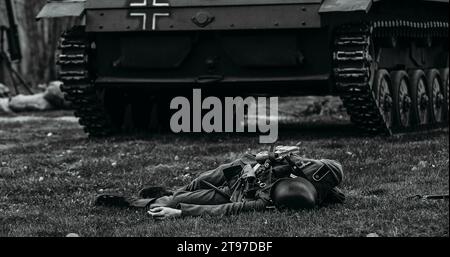 Close Up View on Reenactor, der als deutscher Wehrmachtssoldat gekleidet ist, liegt bei der Rekonstruktion der Schlachten des Zweiten Weltkriegs in der Nähe des leichten Panzerpanzers der Wehrmacht getötet Stockfoto