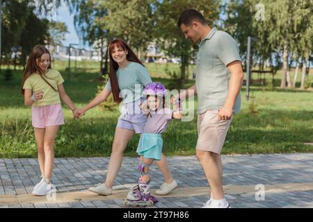 Lächelndes Mädchen Rollschuhlaufen mit Eltern und Schwester im Park Stockfoto