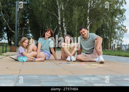 Lächelnde Familie, die auf dem Fußweg im Park sitzt und genießt Stockfoto